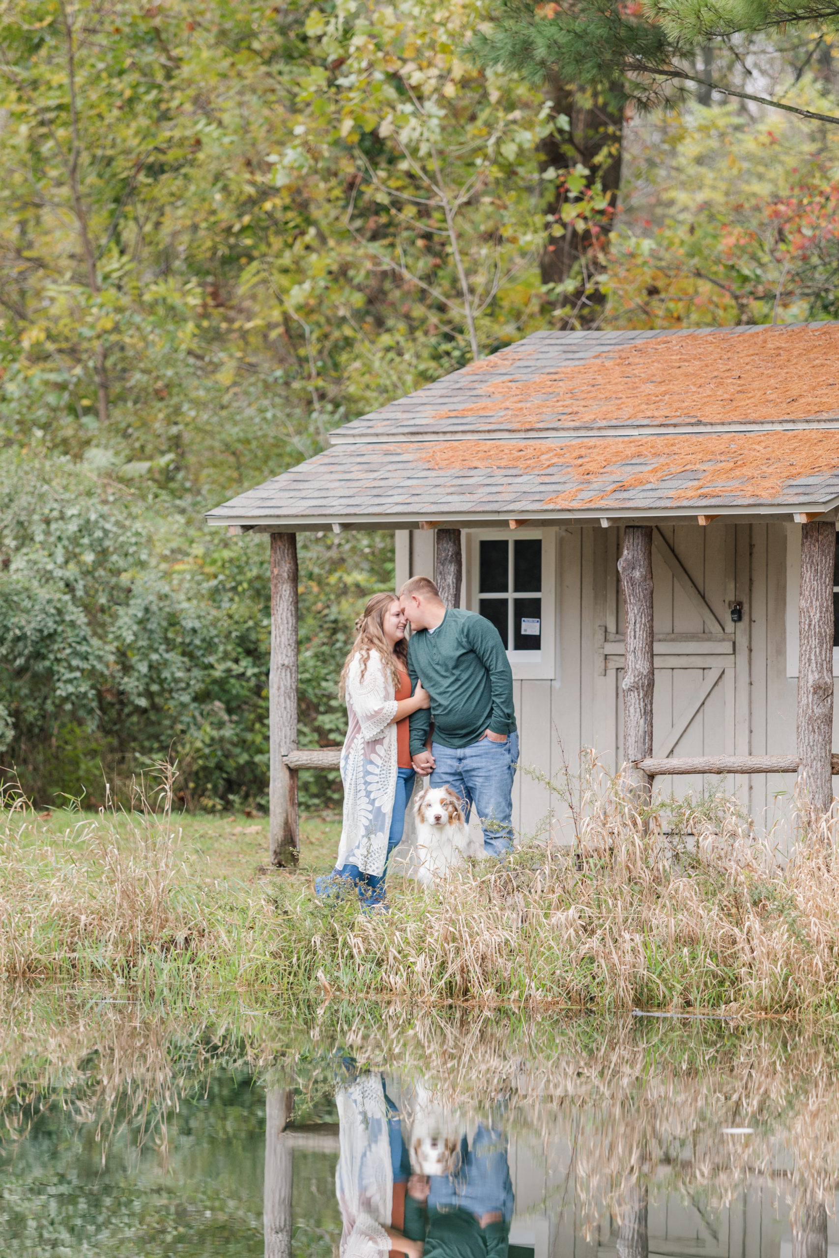 couple posing with their dog in front of a lake house