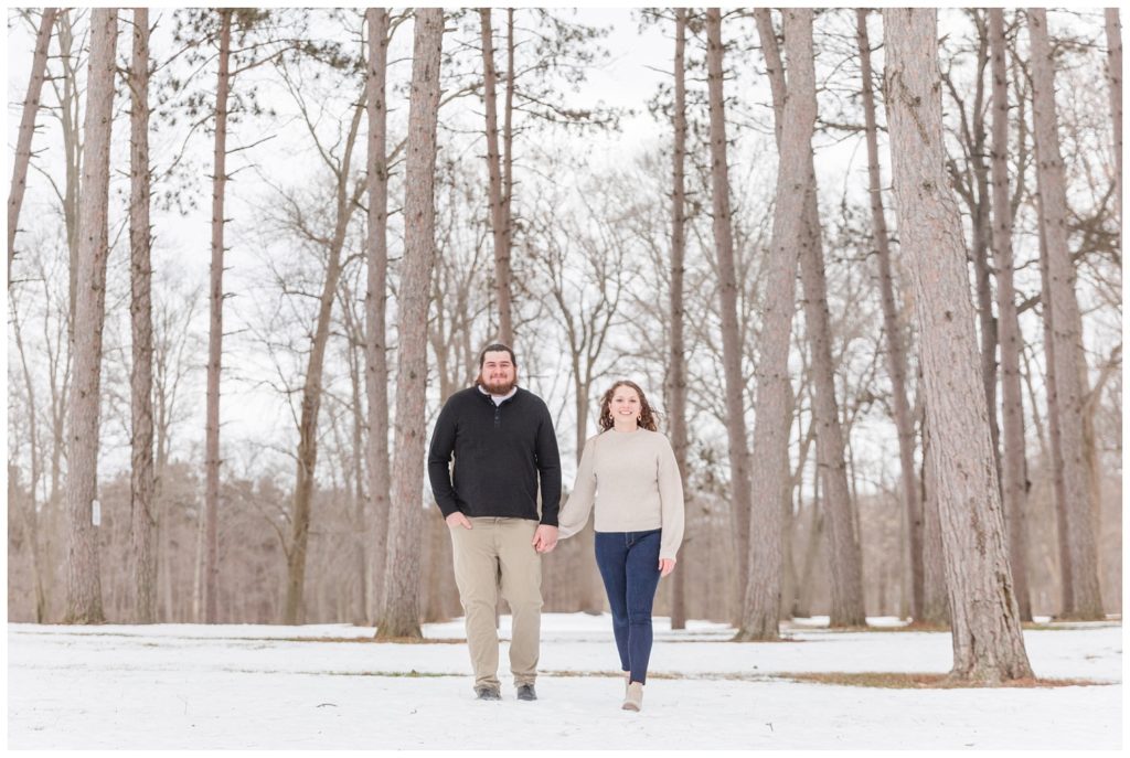 couple holding hands and looking at the camera in front of trees and snow
