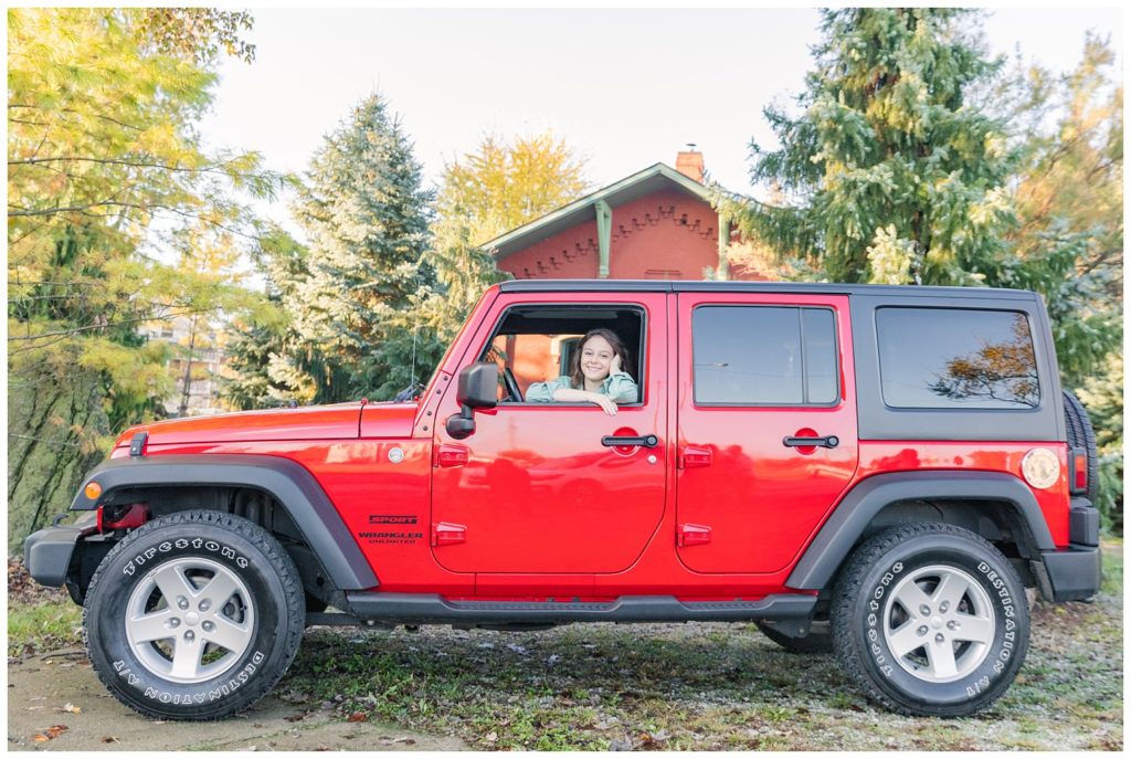 girl posing in her red jeep outside for senior photos