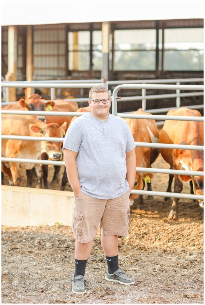 senior boy standing in front of cows on his farm in Ohio