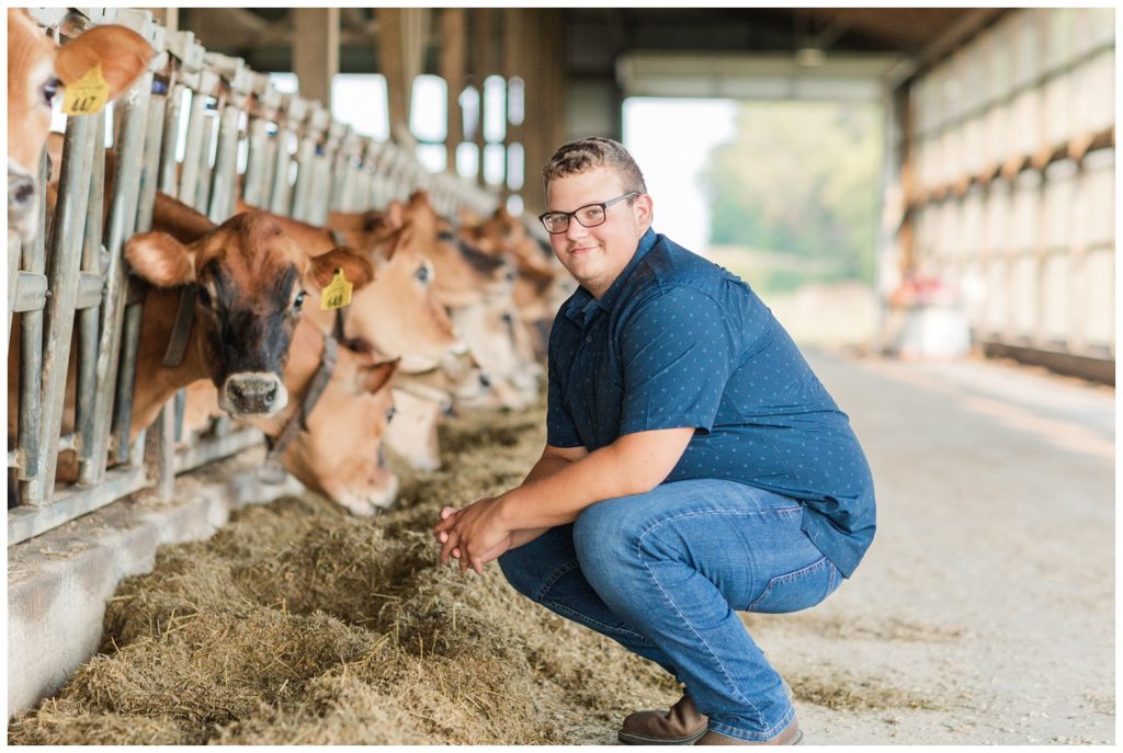 boy kneeling in front of his cows for his senior photoshoot