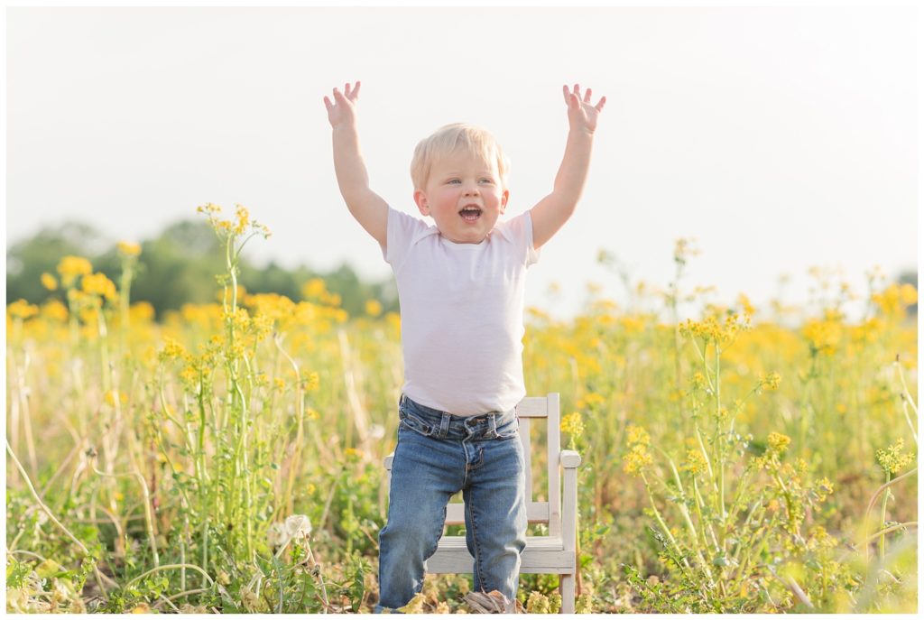 little boy throwing his hands up in the air in a yellow field