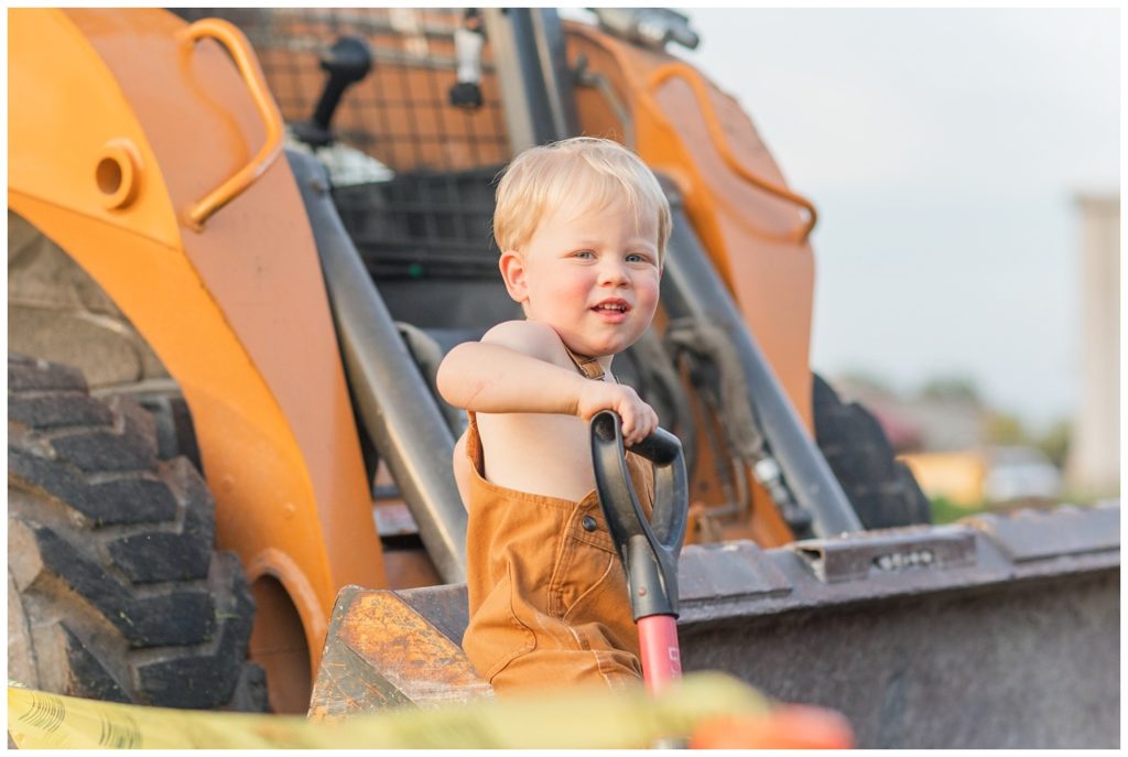 boy holding a shovel while sitting inside the bucket of a side loader