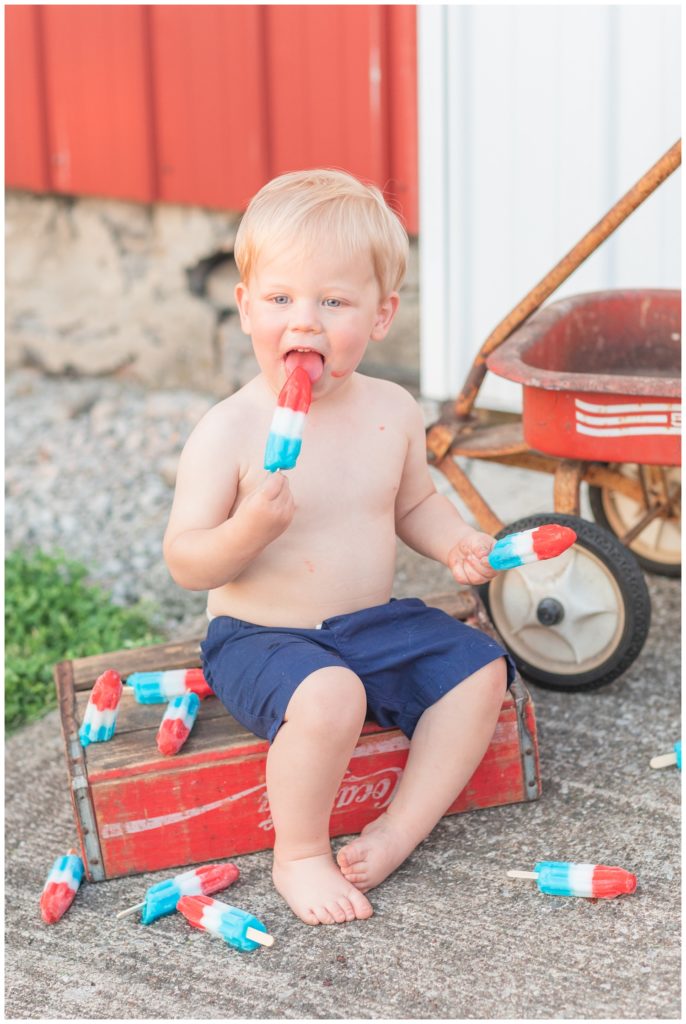 little boy wearing blue shorts and eating a popsicle outside 