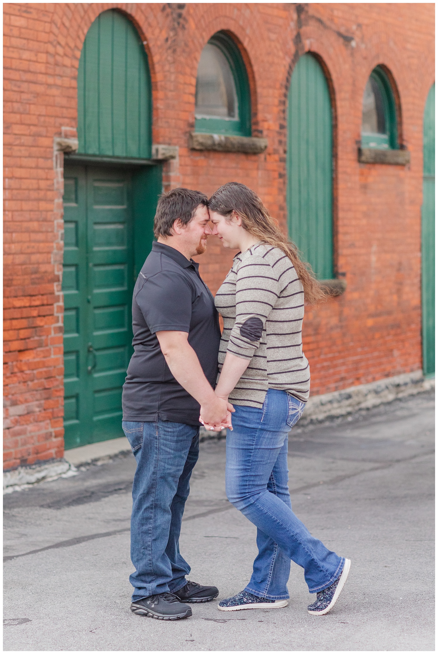 couple posing in front of a red brick building with green doors