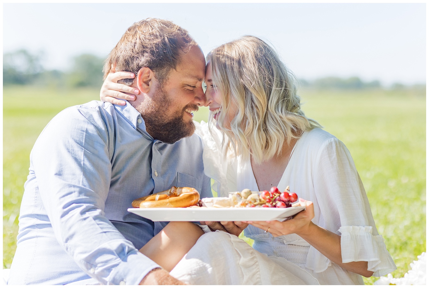 couple sitting together and eating charcuterie in a field