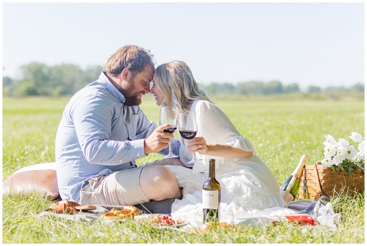couple sitting together and toasting wine in a field 