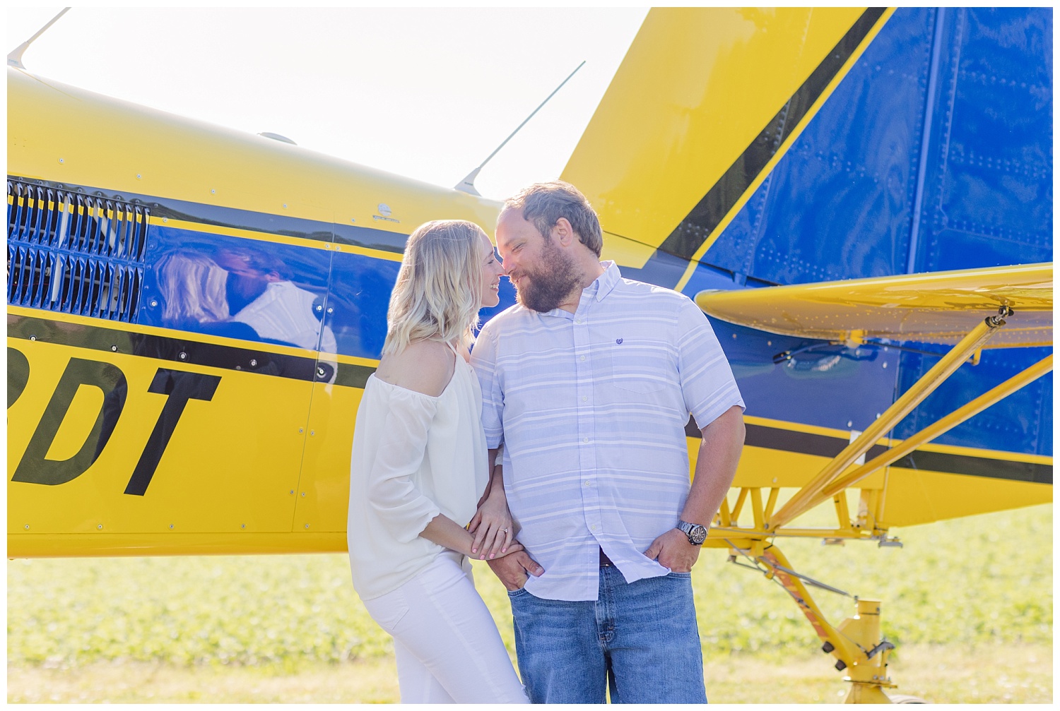 couple standing in front of a yellow and blue airplane during engagement session