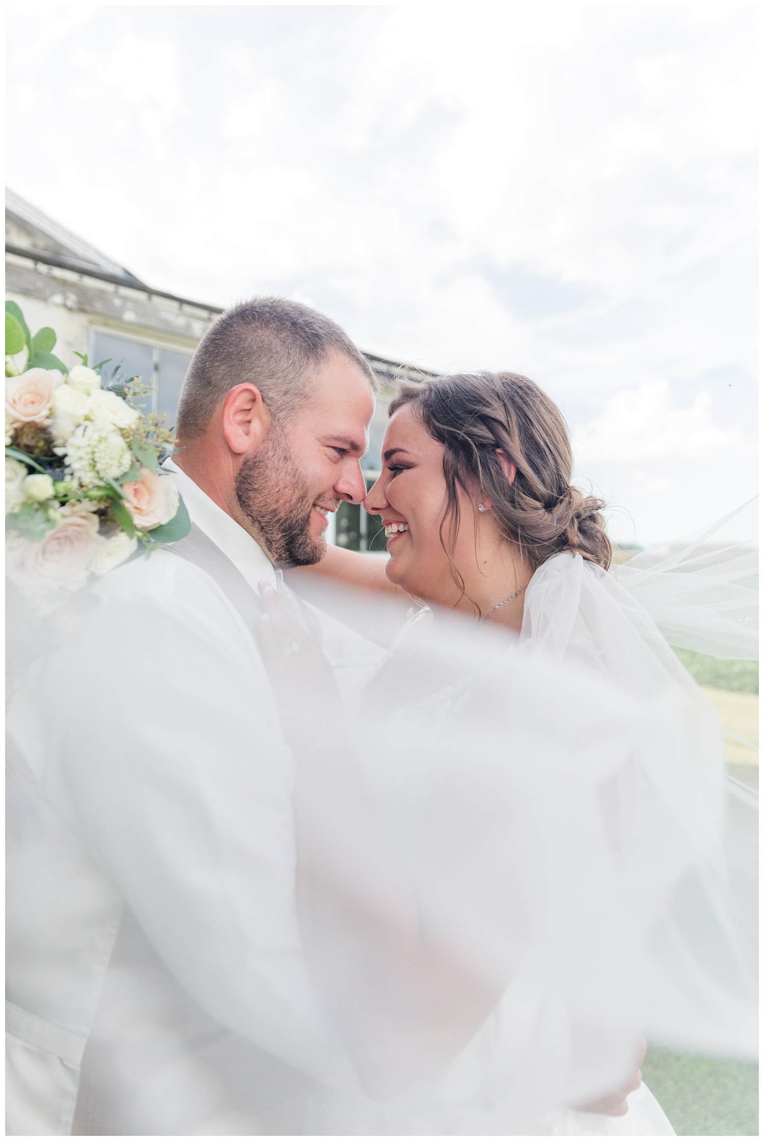 veil wrapped around a wedding couple for photos on a farm