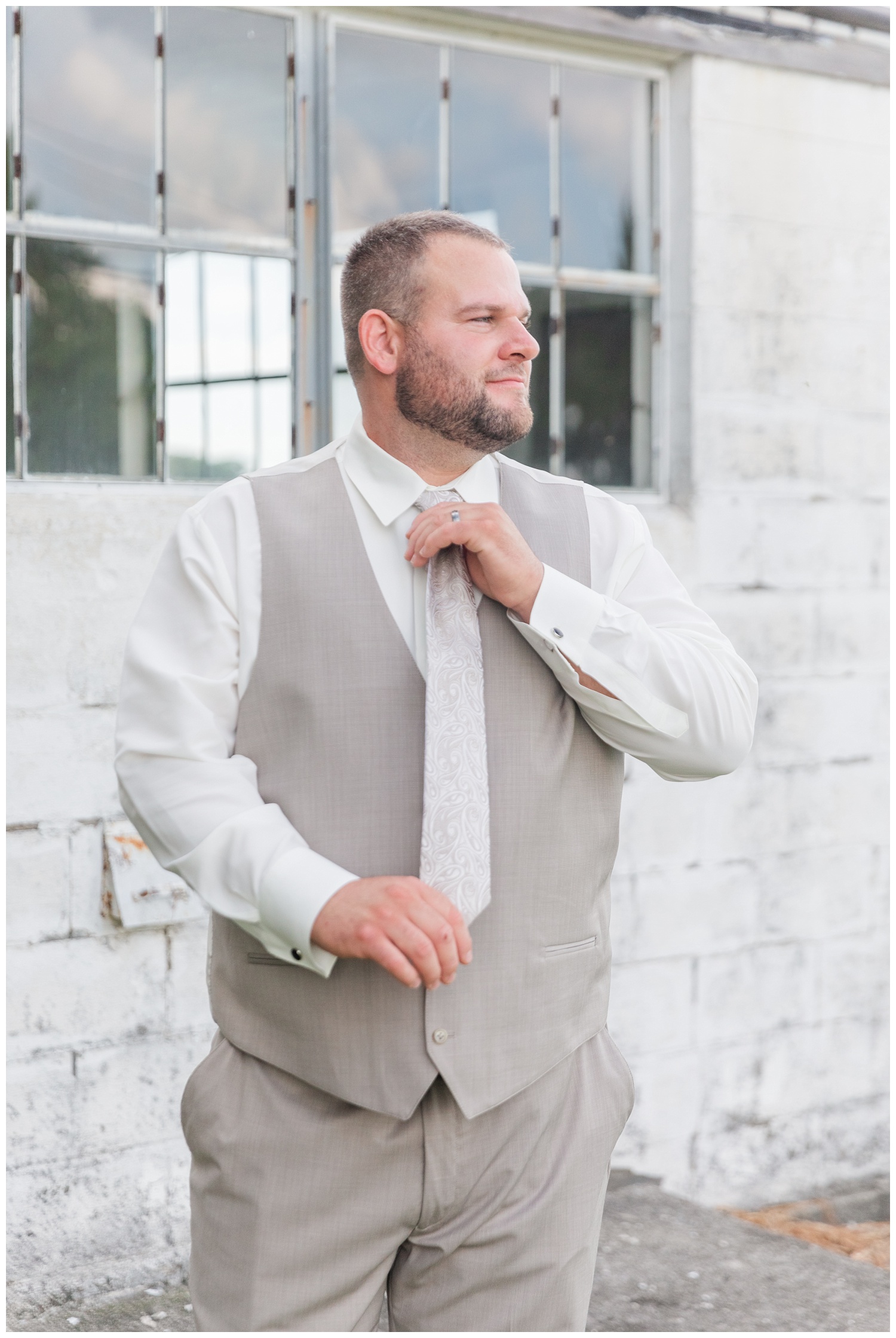 groom adjusting his tie in front of a white barn in Fremont, Ohio