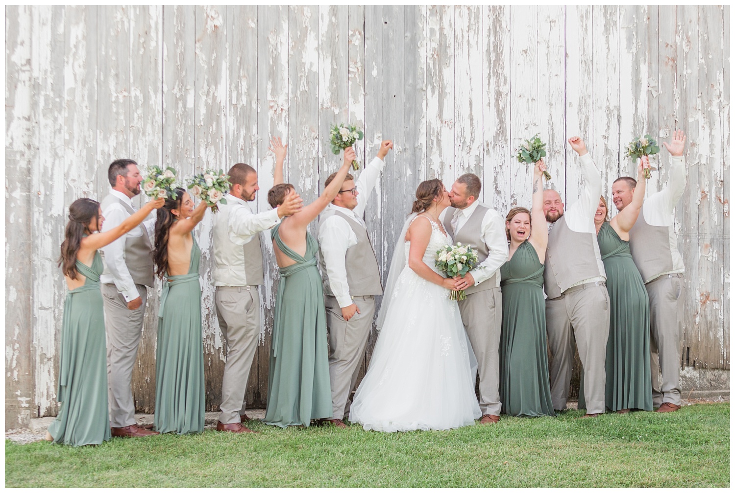 full bridal party posing in front of a white barn