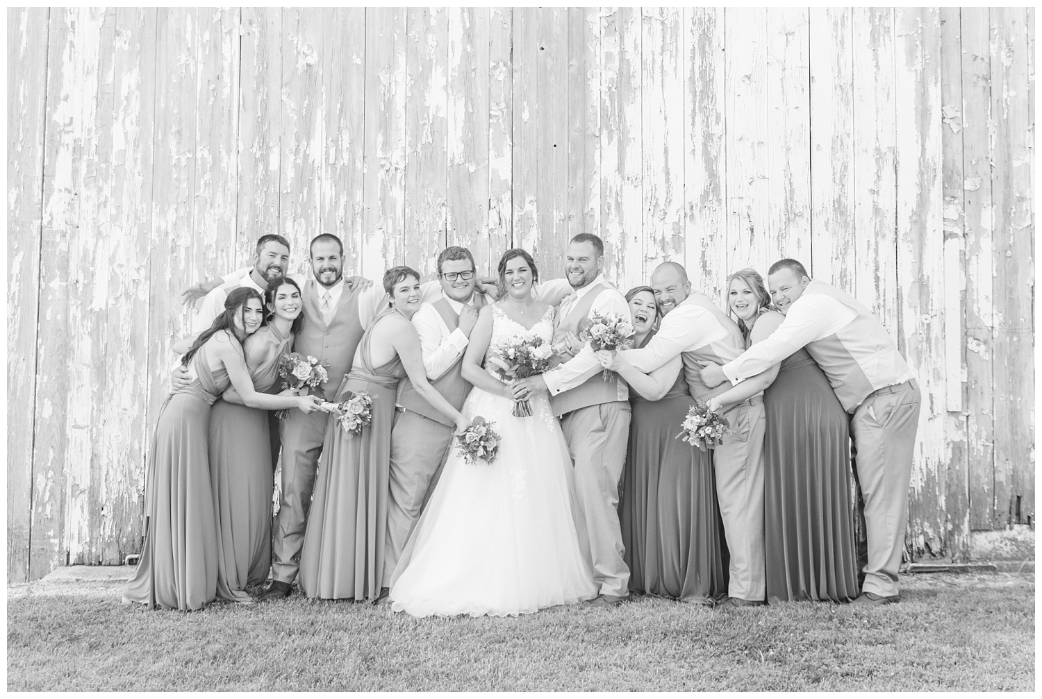 full bridal party posing in front of a white barn
