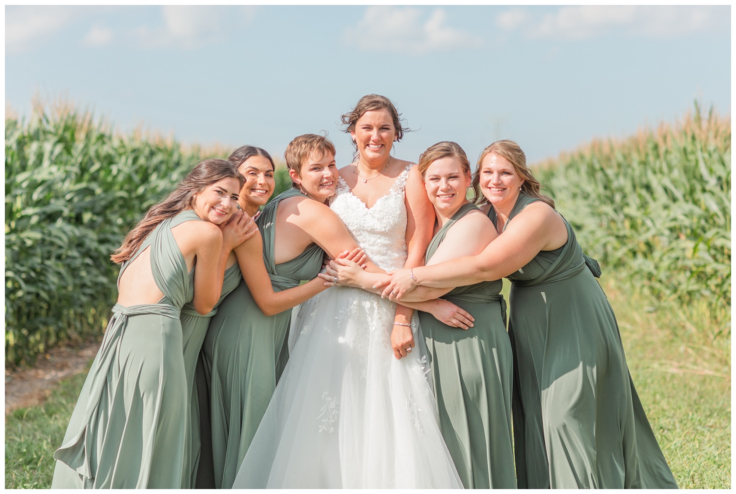 bridesmaids hugging bride in between corn stalks in Fremont, Ohio