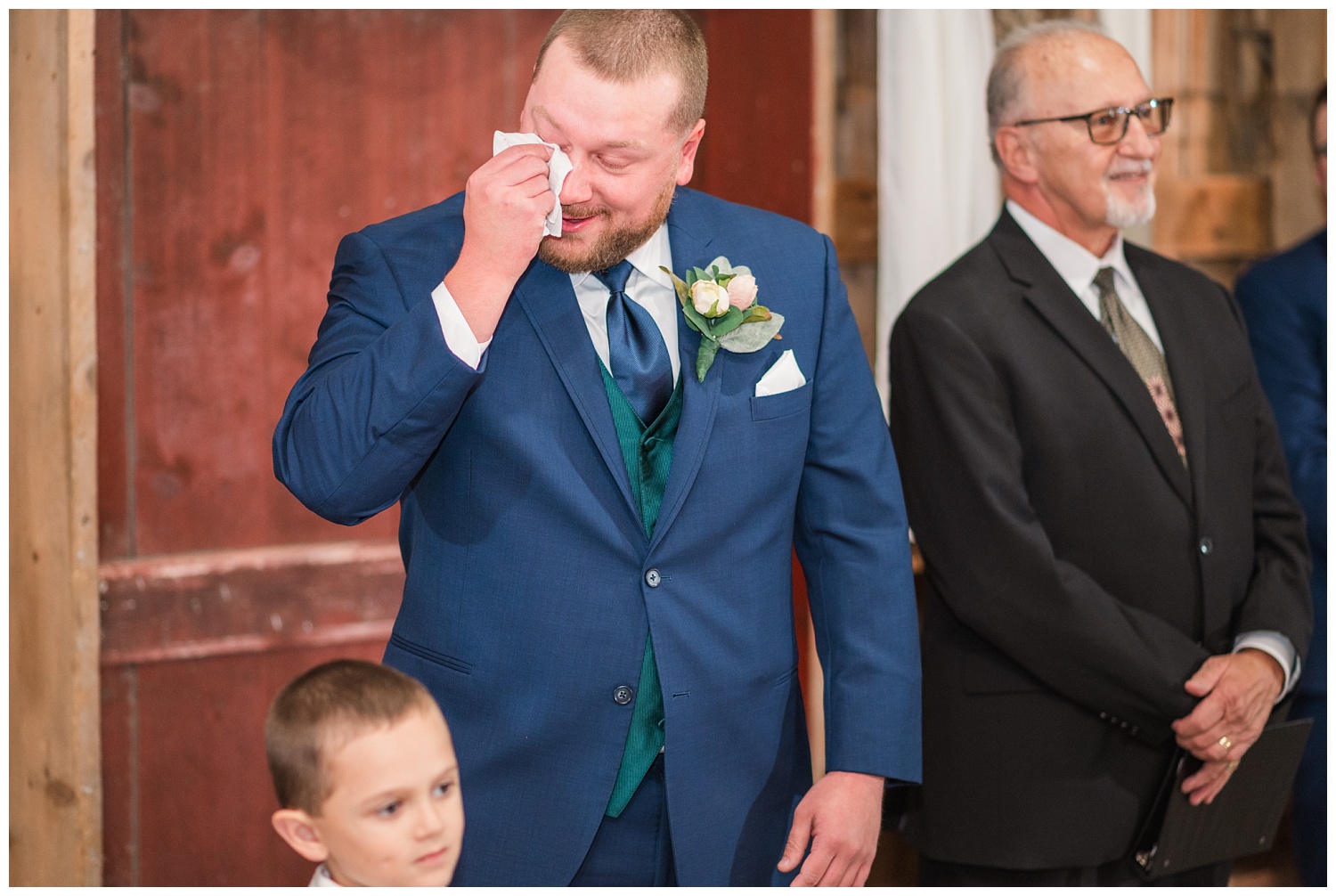 groom wiping away tears while watching bride walk down the aisle