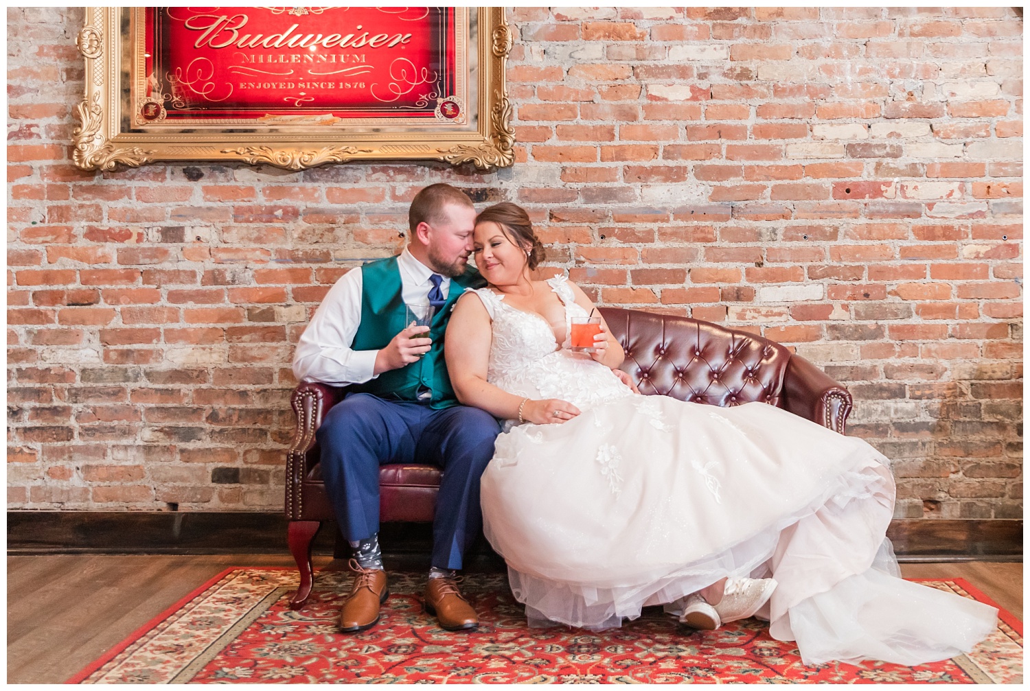 bride and groom sitting with drinks on a leather couch