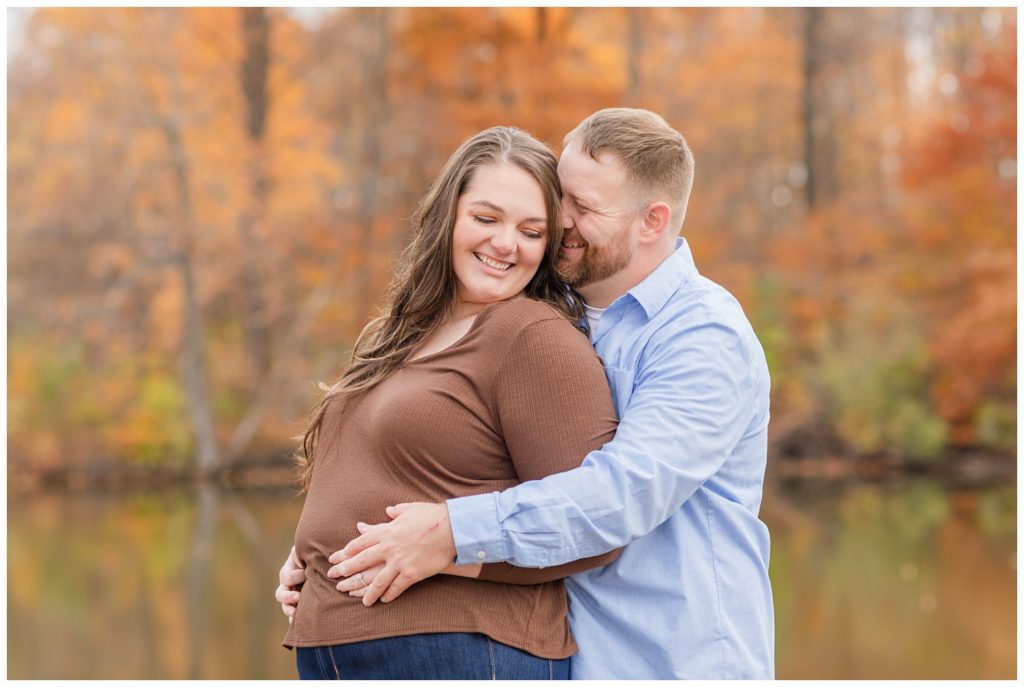 couple hugging next a pond and trees in the fall