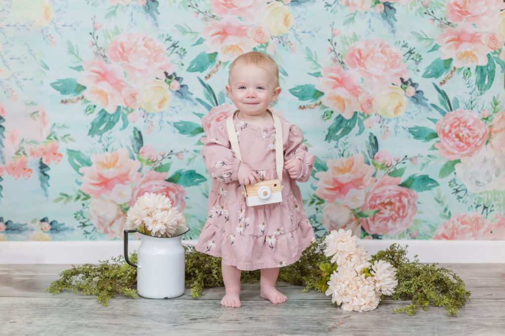little girl standing in front of a floral background wearing a pink dress