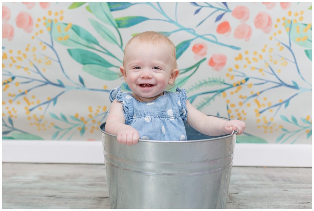 one year old girl sitting on a metal tub at cake smash session