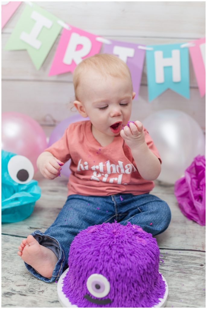 one year old birthday girl eating purple cake on the floor in Fremont, Ohio