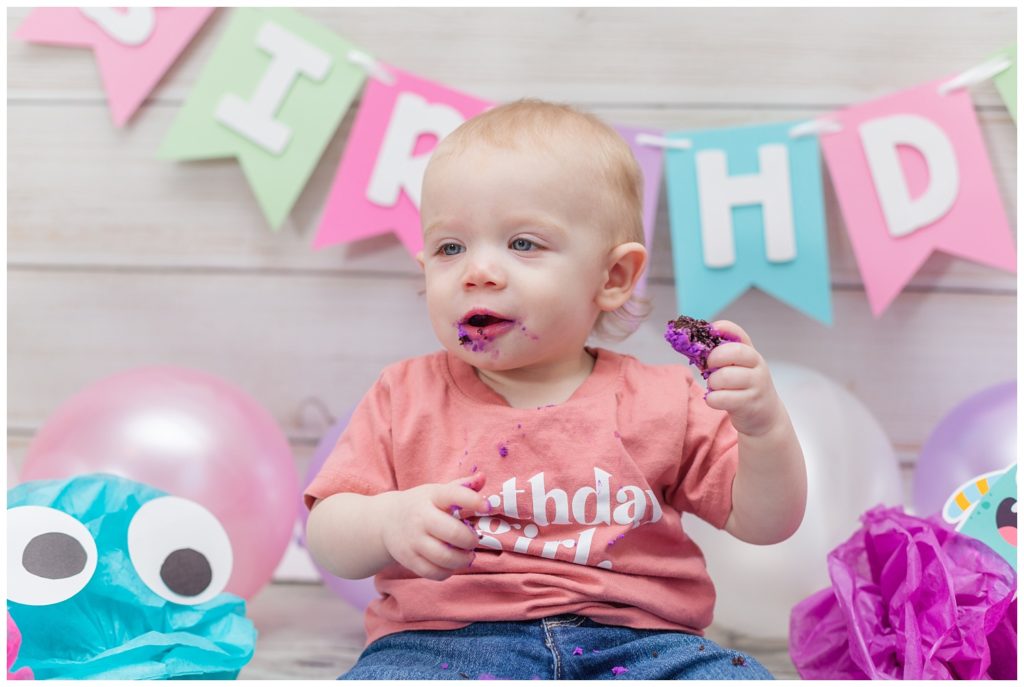 little girl eating chocolate birthday cake at one year photo session