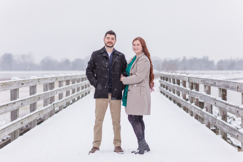 engaged couple standing on a bridge in the snow