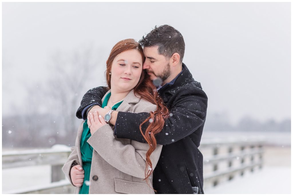 engaged couple hugging on a bridge at Norwalk Reservoir in the snow