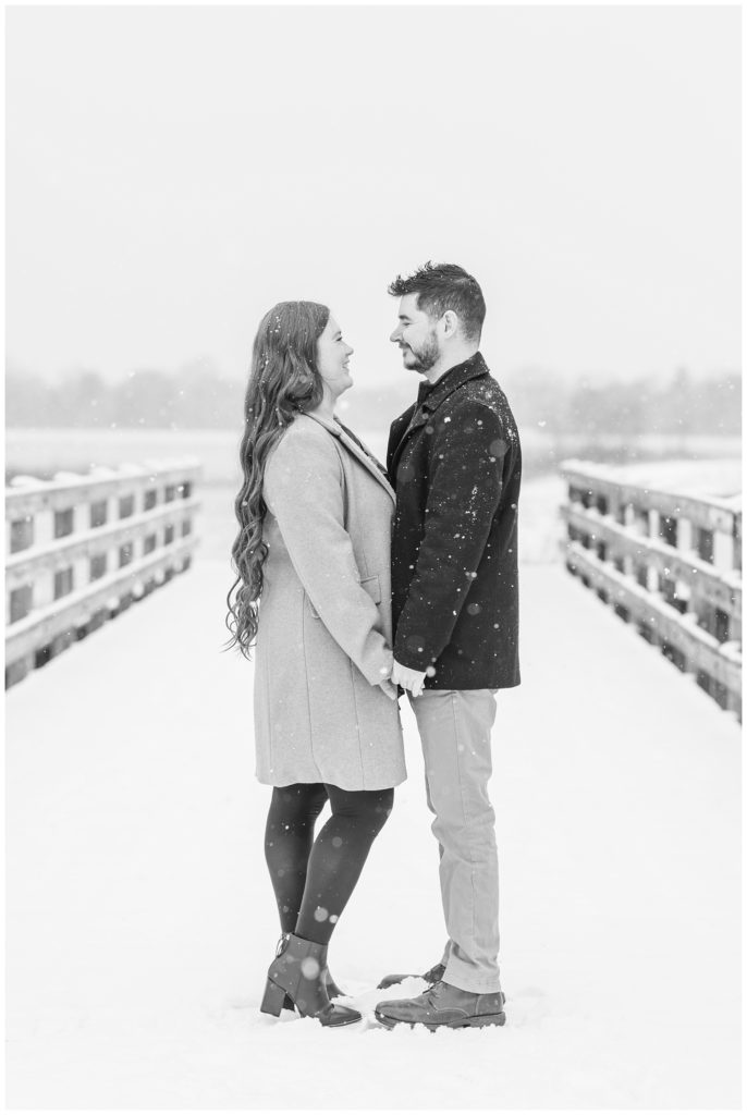 engaged couple standing on a bridge at Norwalk Reservoir in the snow