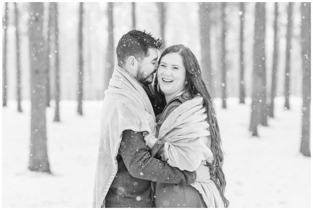engaged couple wrapped in a blanket for snowy engagement session
