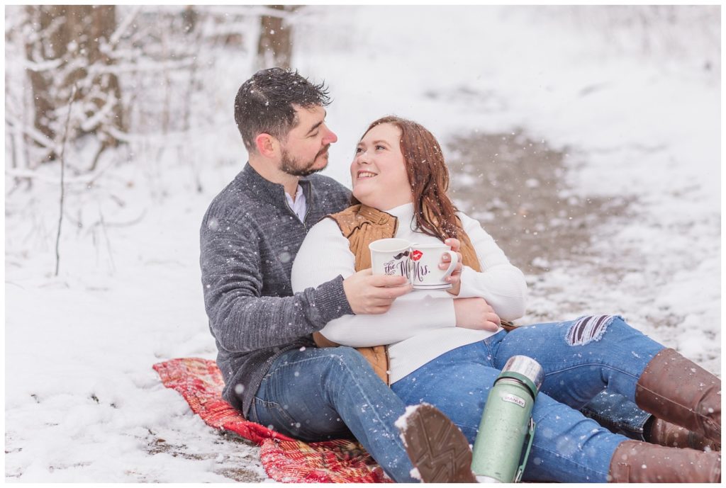 couple sitting in the snow with coffee mugs at engagement session in Ohio
