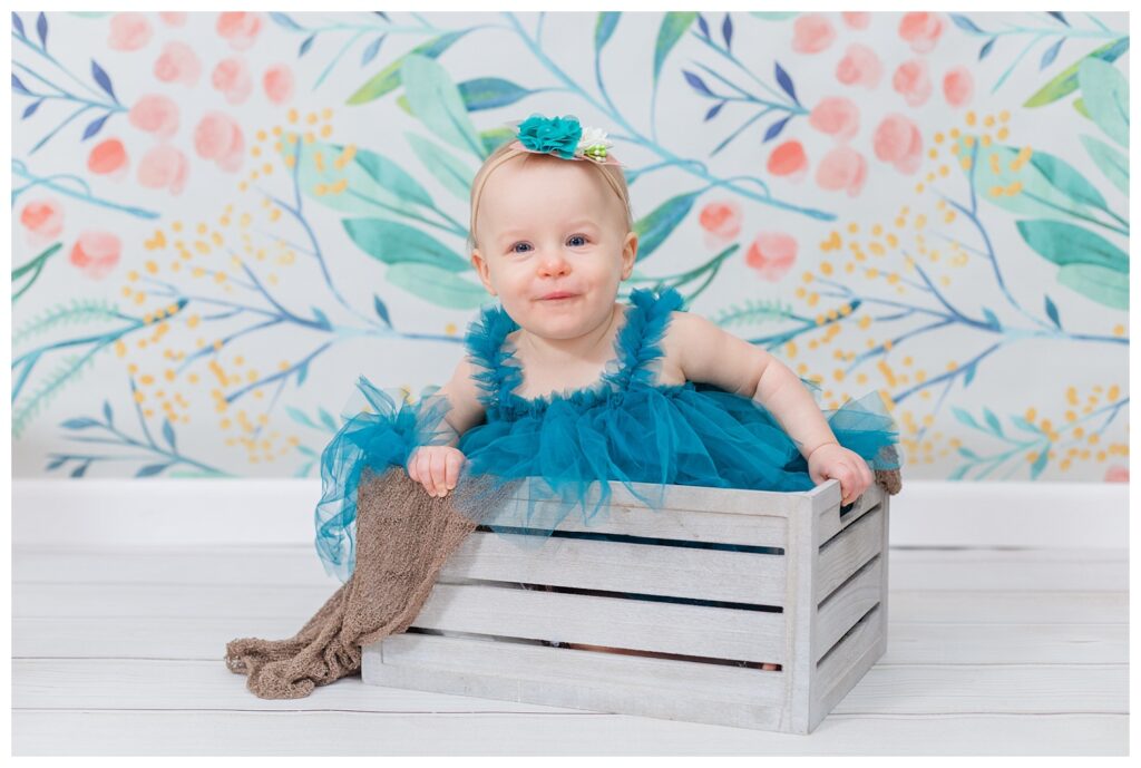 baby girl sitting in a gray crate wearing a blue dress