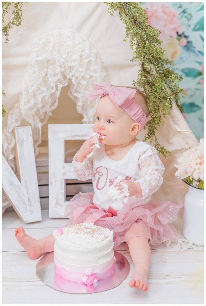 little girl eating a pink and white cake at photo session