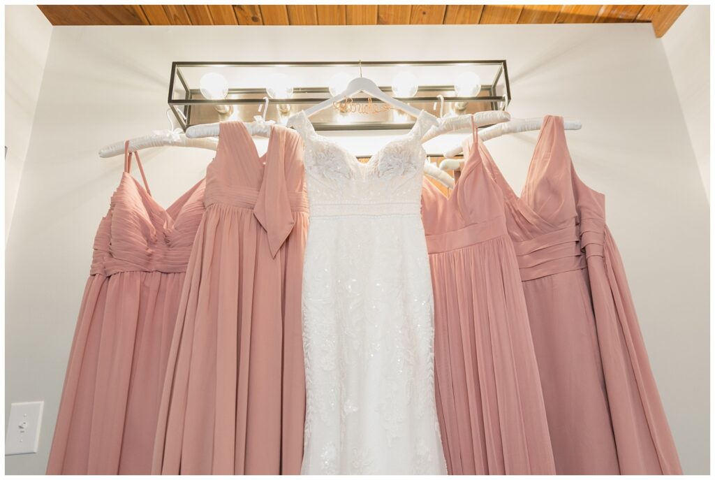 wedding gown and bridesmaids dresses hanging from a light 