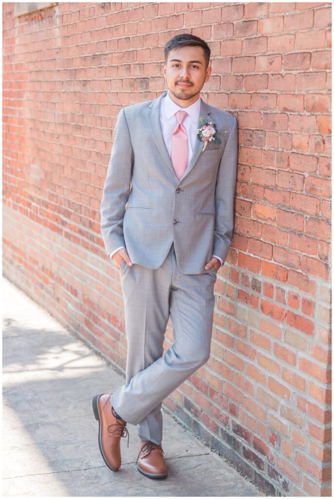 groom posing against a red brick wall in downtown Tiffin