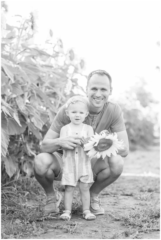 dad kneeling with daughter holding a sunflower on a farm in Ohio
