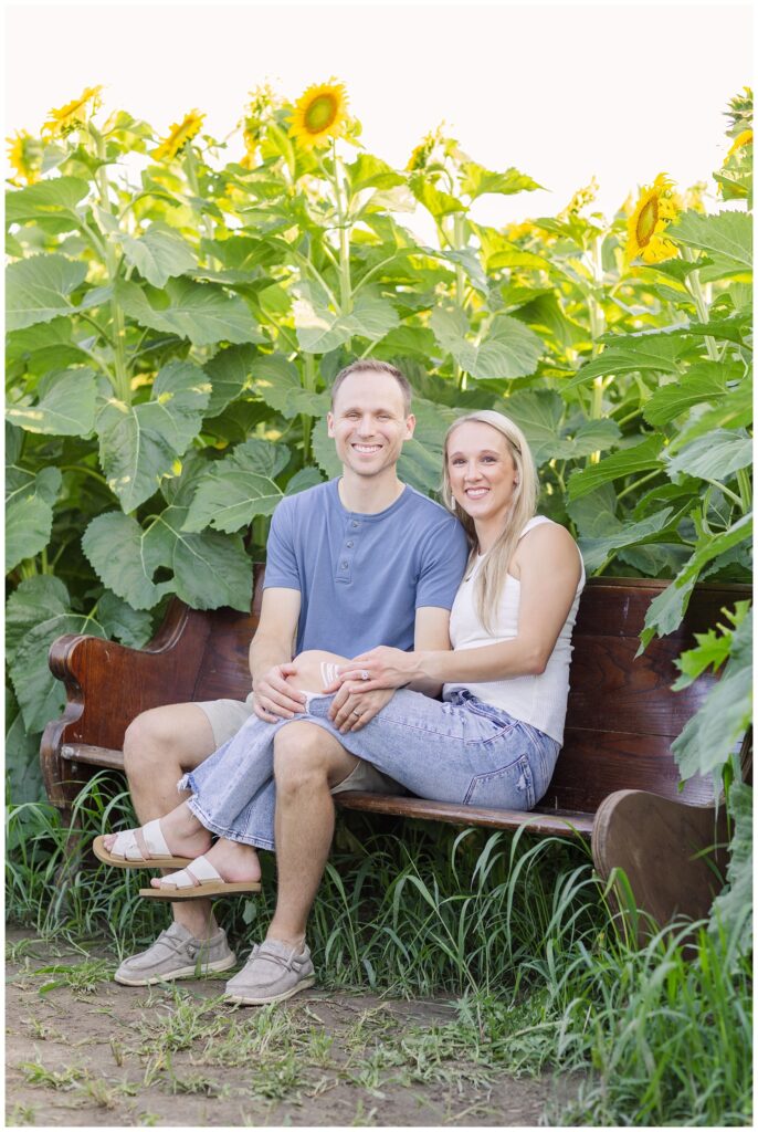 mom and dad sitting on a wooden bench in a sunflower field