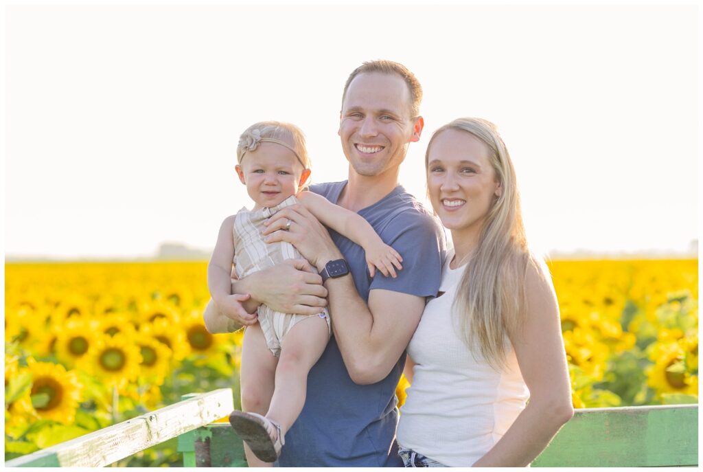 family standing in the back of a truck among a sunflower field