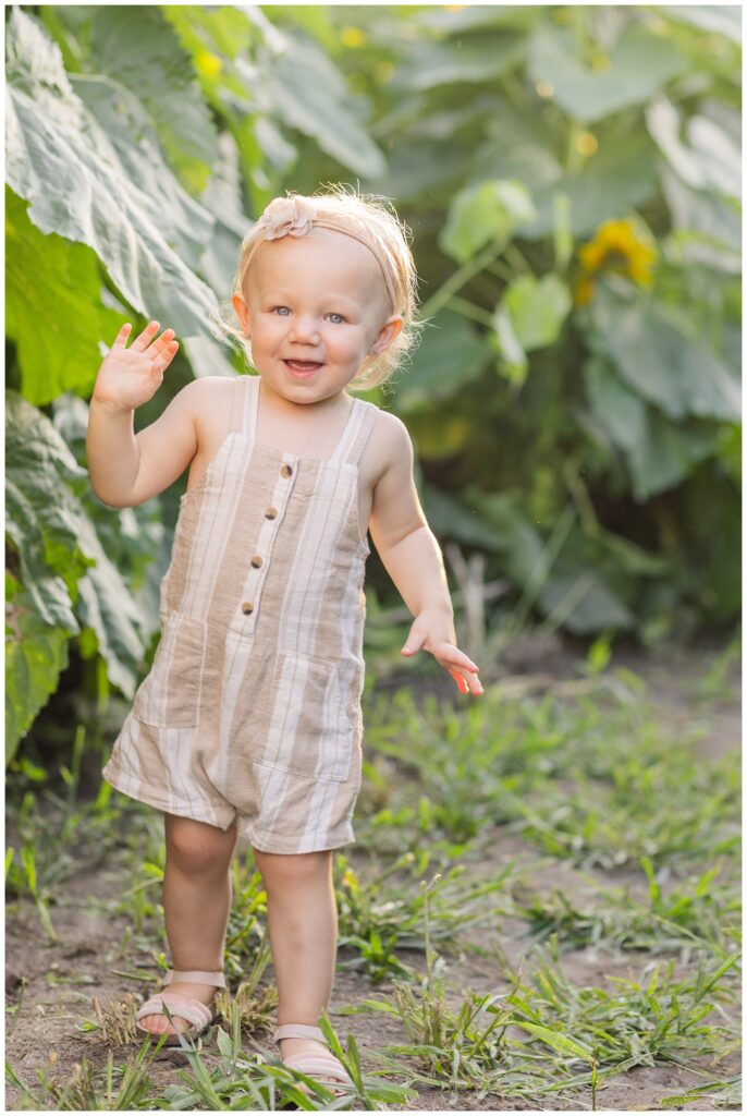 little girl waving while walking in the sunflower field