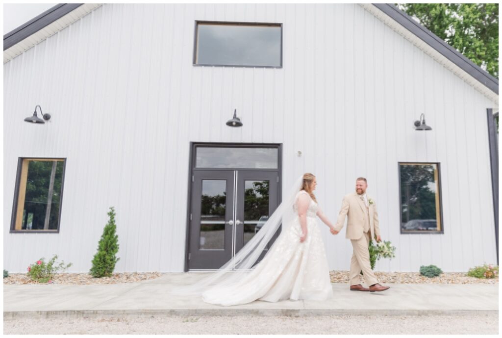bride and groom walking together in front of the Village Barn
