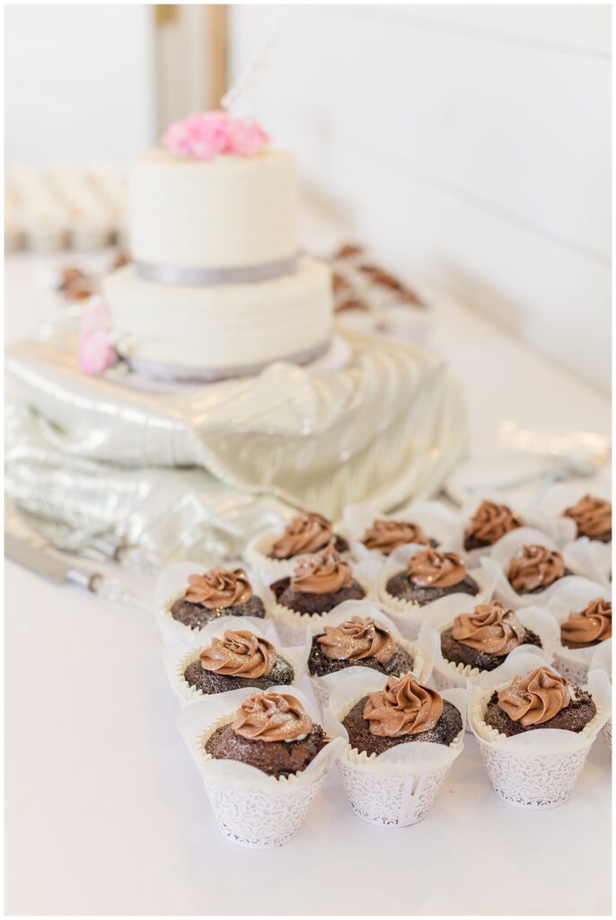 wedding cake and chocolate cupcakes sitting on a table at reception