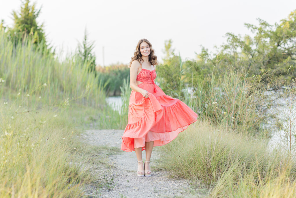 senior wearing a coral dress walking through a field