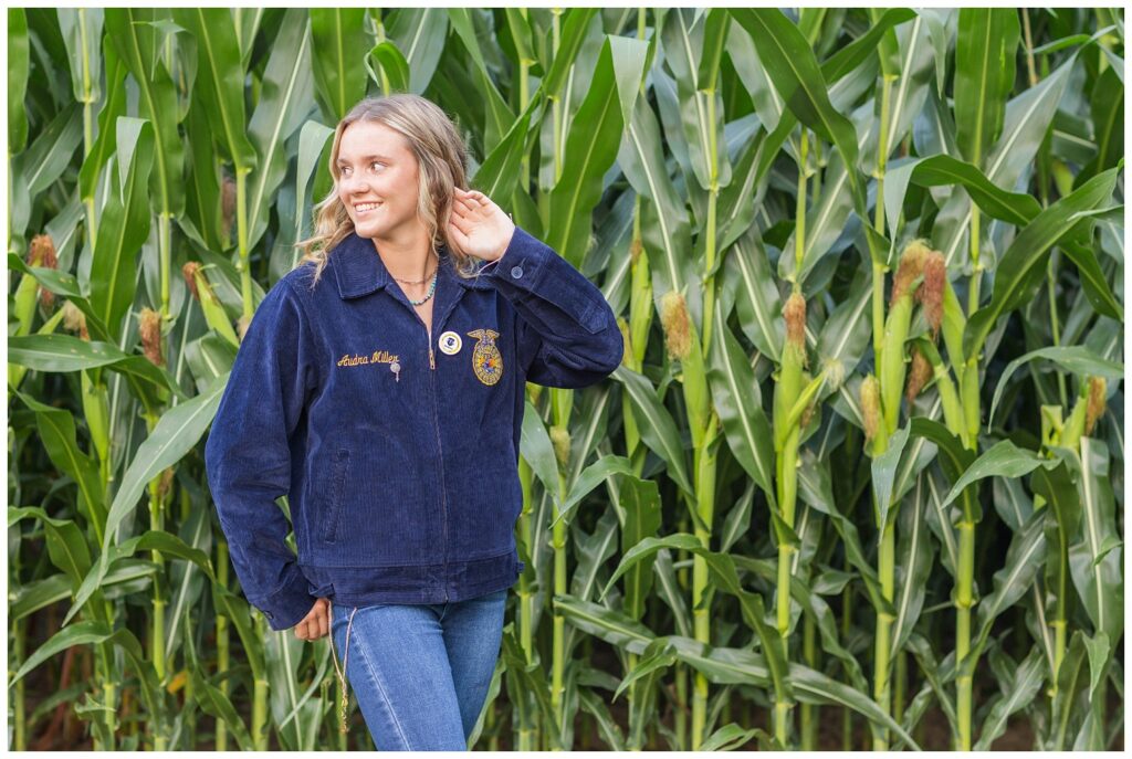 high school senior wearing an FFA jacket standing in front of a corn field