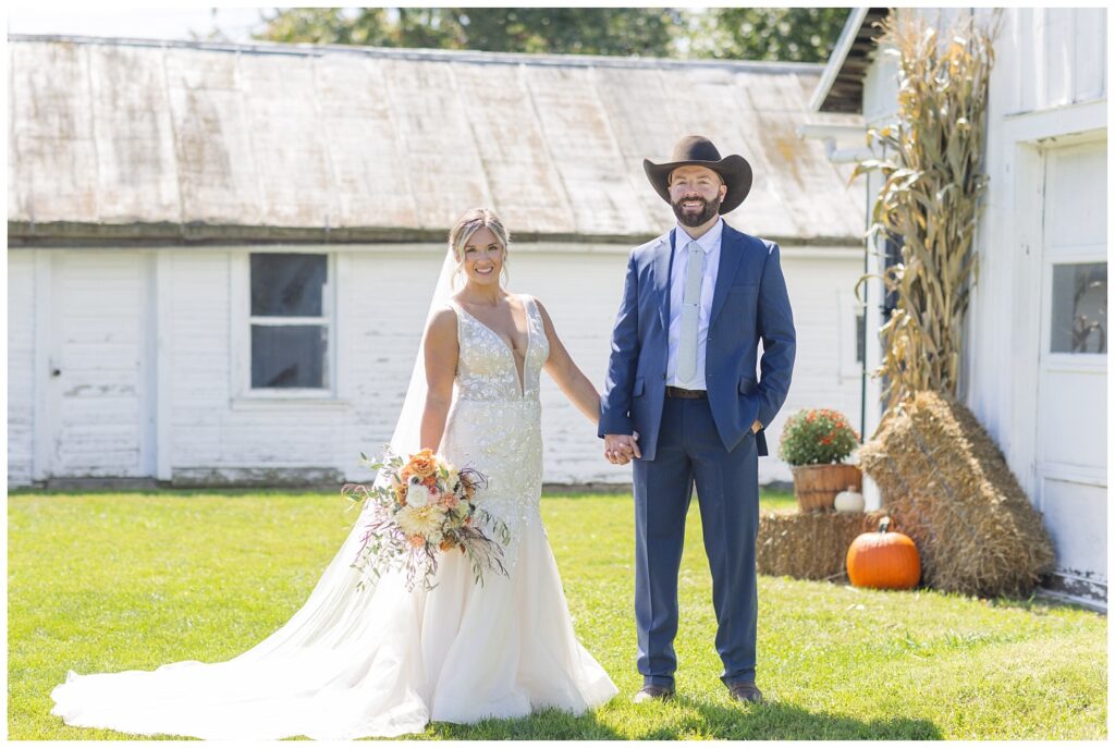 bride and groom holding hands standing next to white barns and fall decorations