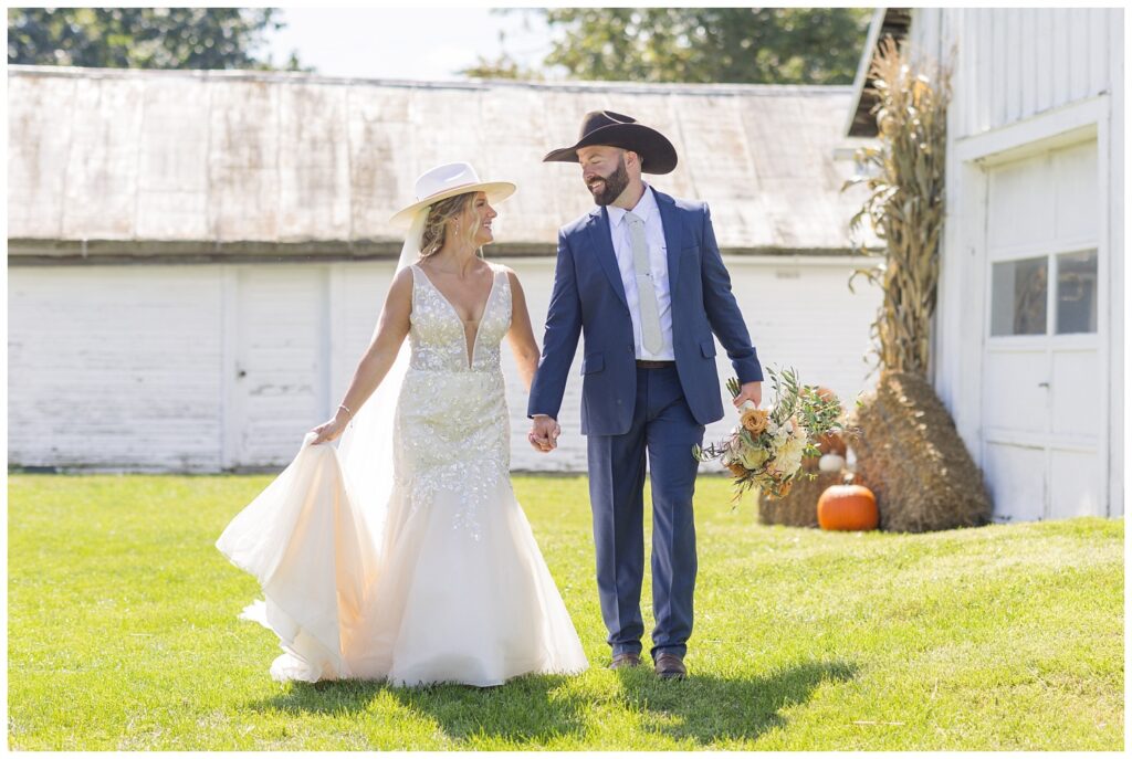 wedding couple walking together in front of a white barn