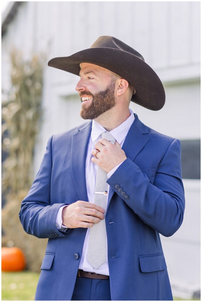 groom wearing a cowboy hat and adjusting his tie at fall Ohio wedding