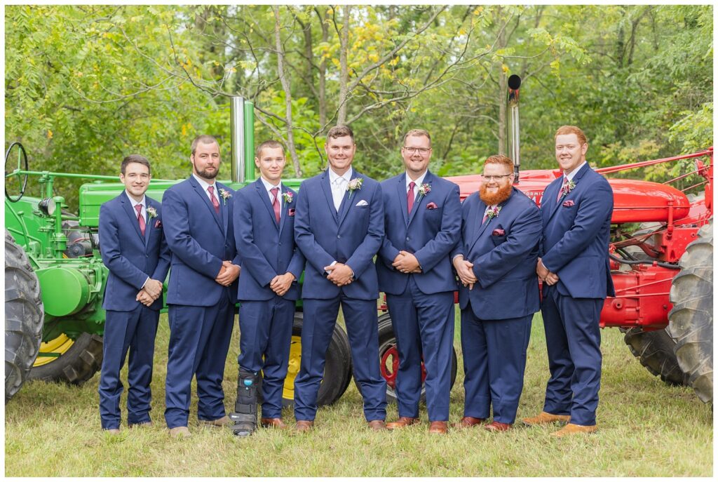 groomsmen posing in front of the groom's red and green tractors