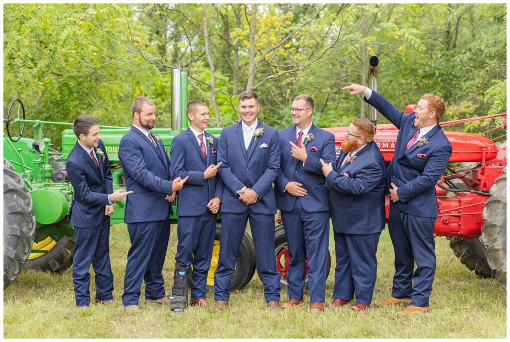 groomsmen posing in front of the groom's red and green tractors