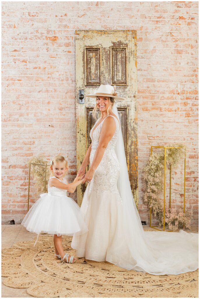 flower girl holding hands with the bride who's wearing a white cowboy hat
