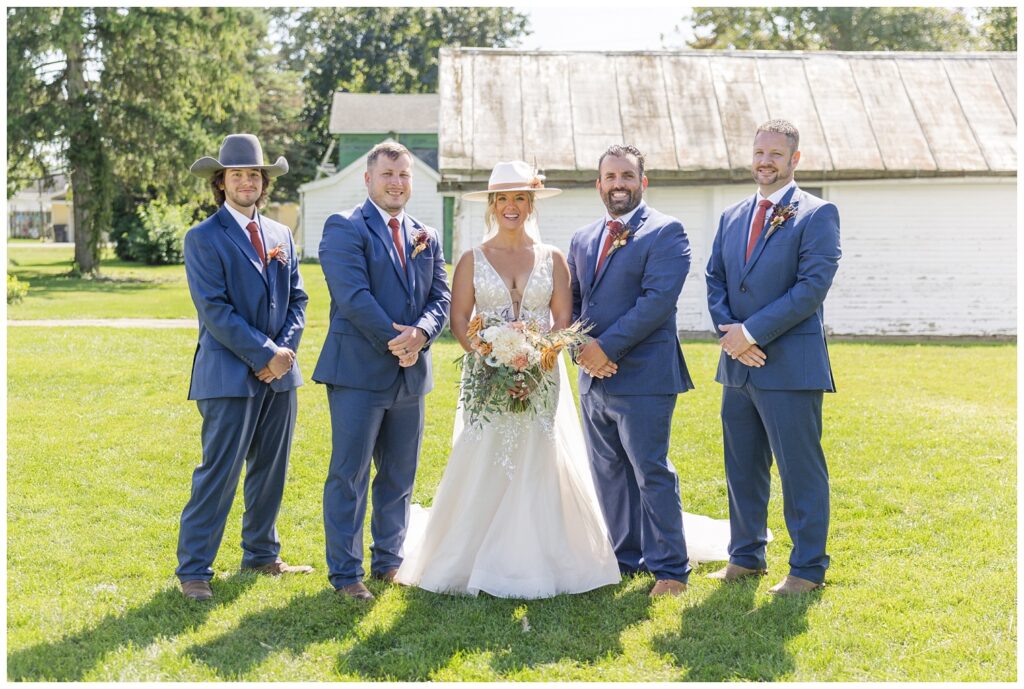 bride posing with groomsmen in front of a white barn in northwest Ohio
