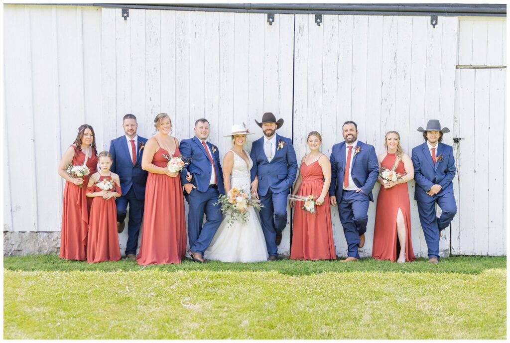 full wedding party posing in front of the white barn at Ole Zim's Wagon Shed venue