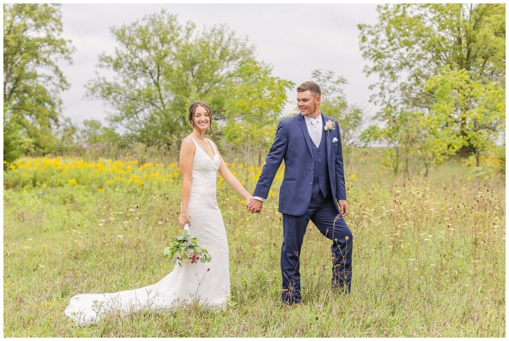bride and groom posing together in a yellow field on their farm 